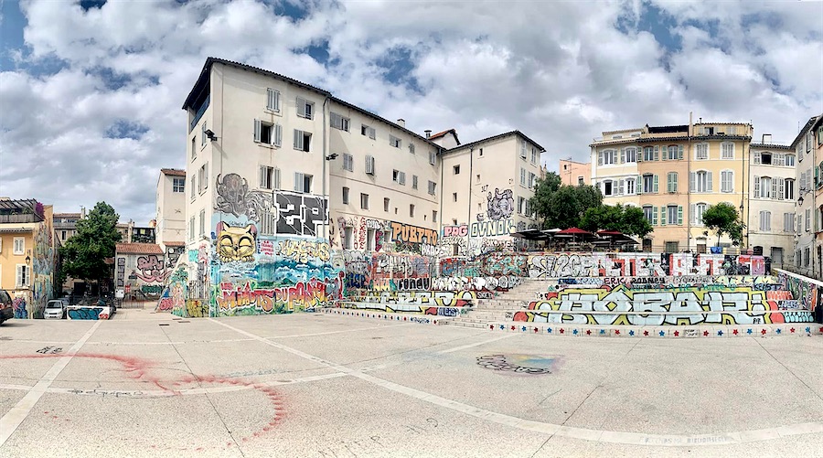 Place bordée d'immeubles dont la base est décorée de graffiti colorés.