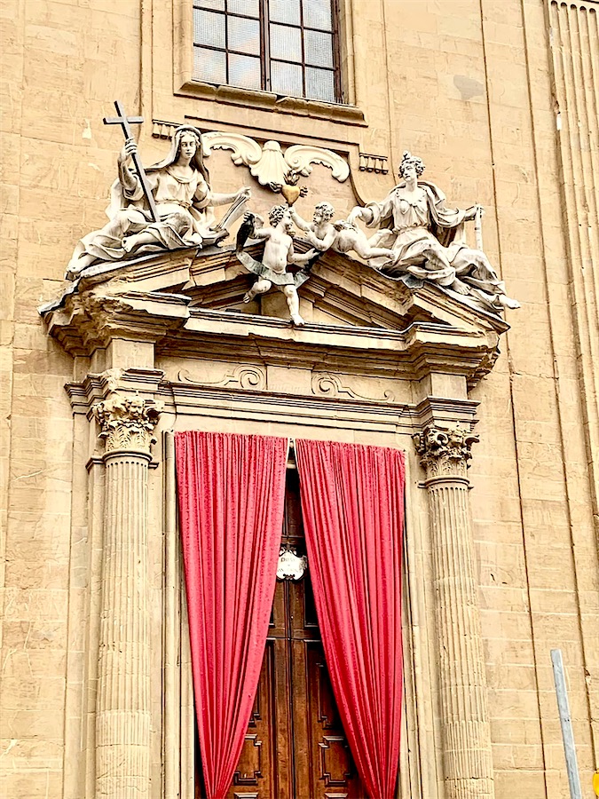 entrée d'un musée, porte tendue d'un rideau rouge, linteau décoré de deux statues et d'angelots, Florence, Italie