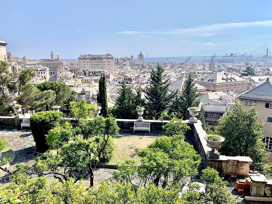 Vue panoramique de Gênes. Au premier plan, un petit parc. et au fond, la ville. Au loin, le port dont on devine les installations portuaires