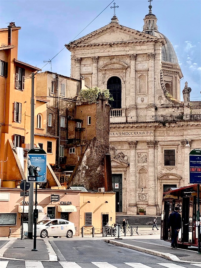 en arrière plan : une église baroque et en premier plan plusieurs construction de forme cubique, Rome