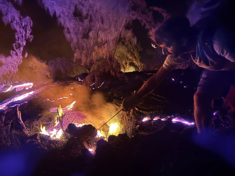 une personne, armée d'une longue baguette, s'approche de la lave incandescente et prélève un peu de lave en fusion