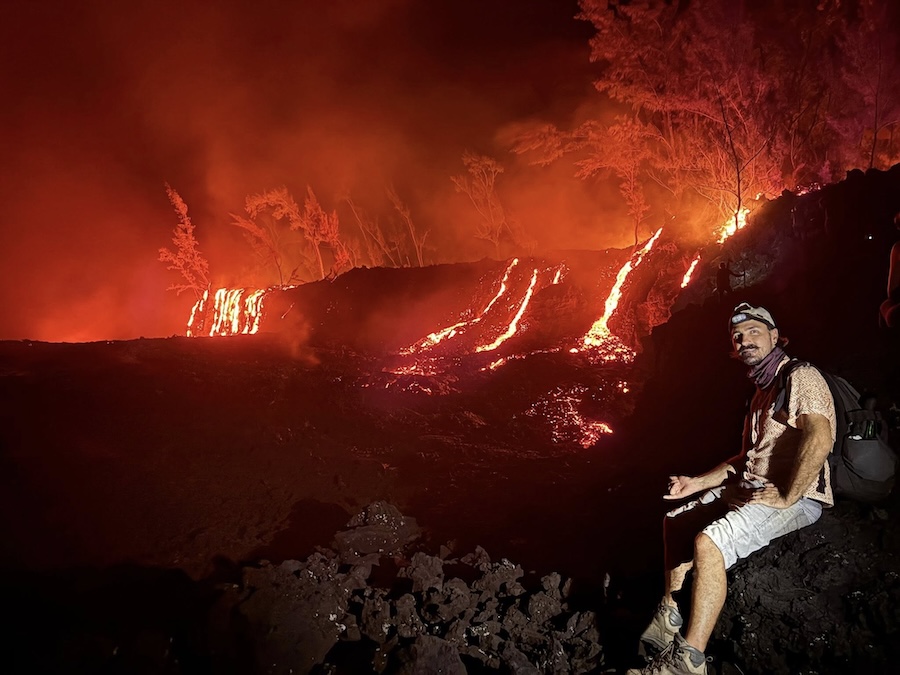 au premier plan, Benoît est assis sur un bloc rocheux et au second plan, coulées de lave en fusion descendant en casdade