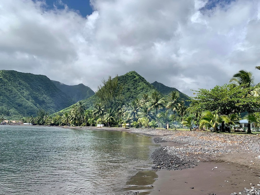 plage au sable gris foncé bordée de cocotiers et, en arrière-plan, des collines verdoyantes, Tahiti
